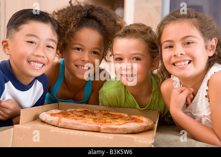 Quatre jeunes enfants à l'intérieur avec pizza smiling Banque D'Images