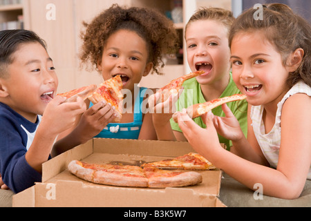 Quatre jeunes enfants à l'intérieur manger pizza smiling Banque D'Images