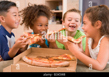 Quatre jeunes enfants à l'intérieur manger pizza smiling Banque D'Images