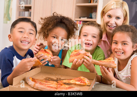 Quatre jeunes enfants à l'intérieur avec woman eating pizza smiling Banque D'Images
