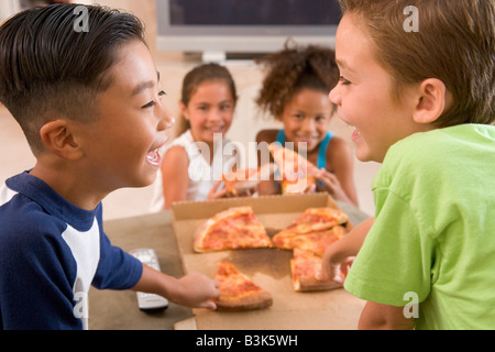 Quatre jeunes enfants à l'intérieur manger pizza smiling Banque D'Images