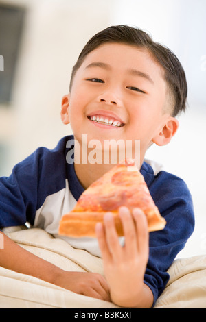 Young boy eating pizza slice in living room smiling Banque D'Images