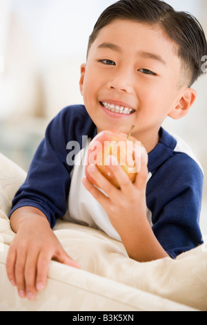 Young boy eating apple dans la salle de séjour smiling Banque D'Images