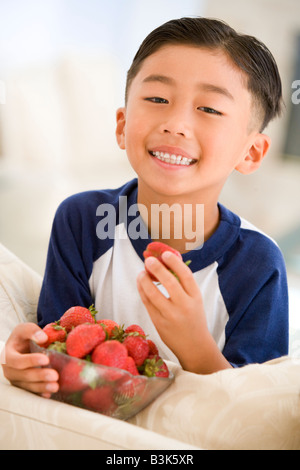 Jeune garçon de manger les fraises au salon smiling Banque D'Images