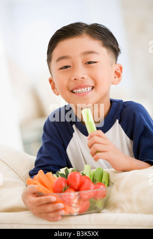 Jeune garçon mangeant bol de légumes frais dans la salle de séjour smiling Banque D'Images