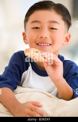 Young boy eating cookie dans salon smiling Banque D'Images