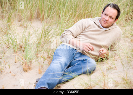 Homme assis sur la plage arrière Banque D'Images