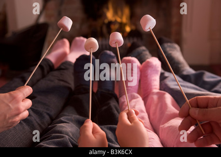 Pieds de réchauffement climatique à la cheminée avec des guimauves sur des bâtons Banque D'Images