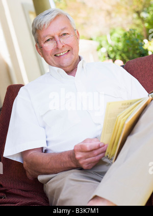 Senior woman sitting en plein air sur une chaise en lisant un livre Banque D'Images