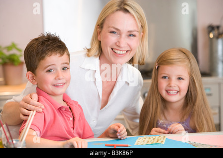 Femme et deux jeunes enfants en cuisine avec un projet d'art smiling Banque D'Images