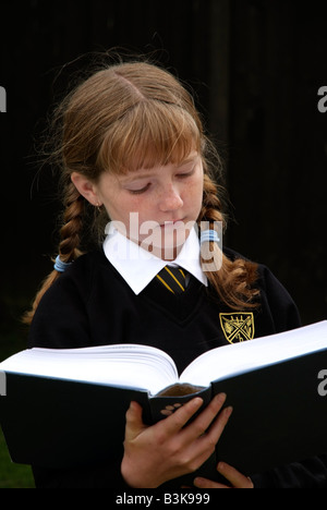 Écolière avec auburn cheveux tressés la lecture d'un livre scolaire Banque D'Images