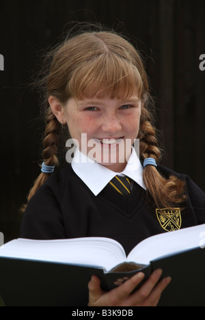 Smiling écolière avec auburn cheveux tressés la lecture d'un livre scolaire Banque D'Images