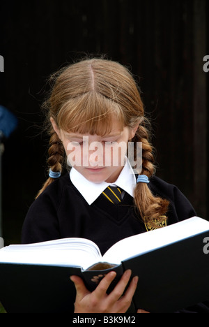 Écolière avec auburn cheveux tressés la lecture d'un livre scolaire Banque D'Images