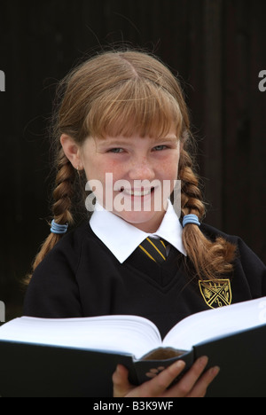 Happy smiling écolière avec auburn cheveux tressés la lecture d'un livre scolaire Banque D'Images