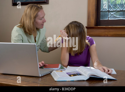 Une mère aide sa fille adolescent en difficulté avec l'école devoirs avec un ordinateur portable sur la table. Banque D'Images