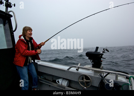 Pêcheur à la femme avec des sentiments partagés de terreur et de plaisir tout en jouant son premier saumon dans une mer difficile sur un bateau de pêche Banque D'Images