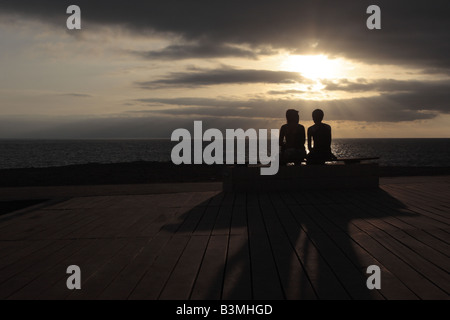 En attendant le coucher du soleil avec un ciel d'orage un jeune couple assis sur un banc sur la promenade à Alcala Banque D'Images