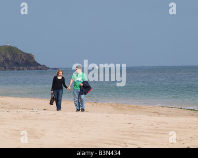 30s en train de marcher le long d'une plage de sable fin, se tenant la main. Banque D'Images