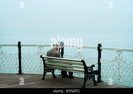 Hauts homme portant veste en tweed et le chapeau est assise sur un banc avec vue sur l'océan sur la jetée de Brighton Brighton, Angleterre Banque D'Images