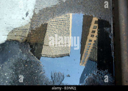 L'immeuble de la Métropolitaine reflété dans une flaque d'eau sur une rue de New York Banque D'Images