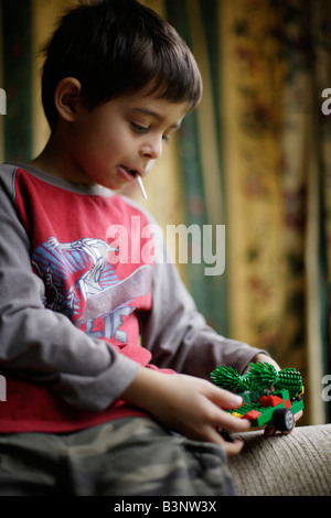 Garçon de 6 ans suce une sucette tout en construisant avec des briques en plastique jouet Banque D'Images