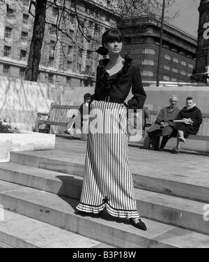 Fashions prises lors de la London Fashion Week 1964 portant blouse et plumeuse Longueur cheville jupe rayée debout sur des mesures concrètes Banque D'Images