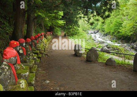 Le Japon, Honshu, la Préfecture de Tochigi. Kanmangafuchi domaine de la ville de Nikko. Les statues de pierre Narabijizo wearing red bavoirs alignés à côté de river Banque D'Images