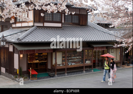 Woman wearing kimono marcher avec ami sous parapluie rouge passé old style boutique à Kyoto pendant la saison des cerisiers en fleur Banque D'Images