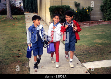 Trois enfants hispaniques à l'école à pied sur la rue de banlieue. Banque D'Images