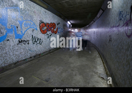 Le métro la nuit, montrant grafitti, avec quatre adolescents (floue) marche à travers Banque D'Images