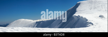 La crête de montagnes d'hiver avec dépassement des plafonds de la neige et des pistes de snowboard sur fond de ciel bleu Banque D'Images