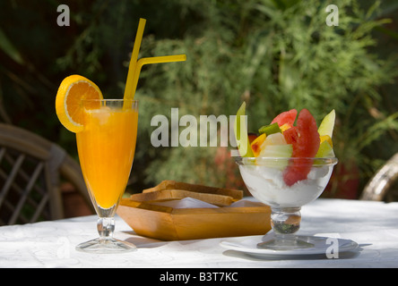 Jus d'Orange, bol de fruits, du pain sur la table de jardin en lin blanc feuillage en plein jour de l'été fond petit-déjeuner Banque D'Images