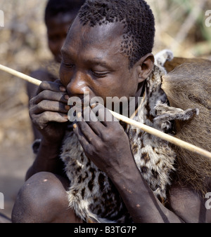 La Tanzanie, le nord de la Tanzanie, le lac Eyasi. Un chasseur Hadza portant comme genet peau de chat cape se redresse une nouvelle flèche l'arbre dans ses dents. Les Hadzabe sont une communauté forte de milliers de chasseurs-cueilleurs qui ont vécu dans le bassin du lac Eyasi depuis des siècles. Ils sont l'un des quatre ou cinq sociétés dans le monde qui continuent de gagner leur vie principalement de ressources sauvages. . Banque D'Images