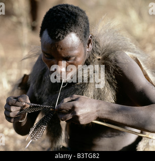 La Tanzanie, le nord de la Tanzanie, le lac Eyasi. Un chasseur Hadza portant une peau de babouin fledges une flèche l'arbre avec des plumes de pintade en utilisant les bases d une antilope.Les Hadzabe sont une communauté forte de milliers de chasseurs-cueilleurs qui ont vécu dans le bassin du lac Eyasi depuis des siècles. Ils sont l'un des quatre ou cinq sociétés dans le monde qui continuent de gagner leur vie principalement de ressources sauvages.. . Banque D'Images