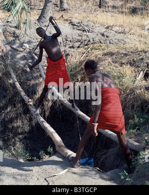 La Tanzanie, le nord de la Tanzanie, de Manyara. Deux jeunes hommes Datoga puits de travail sur le côté est du lac Manyara, à l'eau leur bétail. L'homme qui attire l'eau en équilibre précaire sur deux pôles.L (Datoga connus par leurs voisins comme le Maasai Mang'ati et pour les Iraqws comme Babaraig) vivent dans le nord de la Tanzanie et sont principalement des éleveurs. Banque D'Images