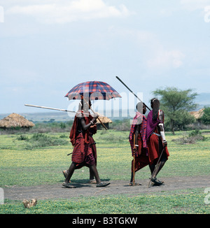 La Tanzanie, le nord de la Tanzanie, Engaruka. Les guerriers Massaïs en tenue traditionnelle avec de longs cheveux tressés et des lances à part quitter le marché du bétail hebdomadaire à Engaruka en Tanzanie du nord. La seule rupture avec la tradition est un parapluie en teintes. Maasai préférés Banque D'Images