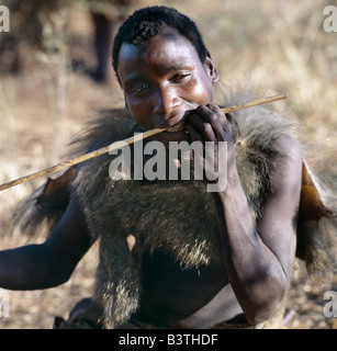 La Tanzanie, Arusha, le lac Eyasi. Un chasseur Hadza portant une cape de peau babouin se redresse une nouvelle flèche l'arbre dans ses dents.Les Hadzabe sont une communauté forte de milliers de chasseurs-cueilleurs qui ont vécu dans le bassin du lac Eyasi depuis des siècles. Ils sont l'un des quatre ou cinq sociétés dans le monde qui continuent de gagner leur vie principalement de ressources sauvages. Banque D'Images