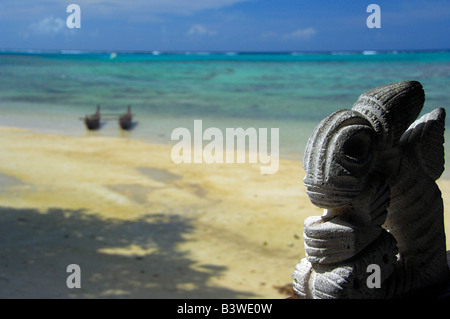 Pacifique Sud, en Polynésie française, Moorea. Tiki en pierre traditionnelle avec double coque canoë sur plage dans la distance. Banque D'Images