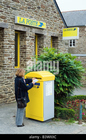 Femme postant du courrier dans la boîte aux lettres pilier devant le bureau de poste, la poste, Plancoët village Bretagne France Europe Banque D'Images