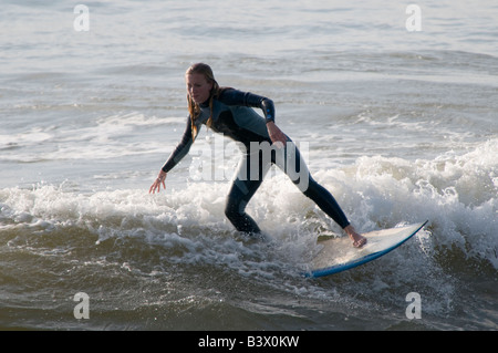 Young blonde woman wearing wetsuit surf sur surf sur les vagues au large de Aberystwyth, Pays de Galles, Royaume-Uni après-midi d'été Banque D'Images