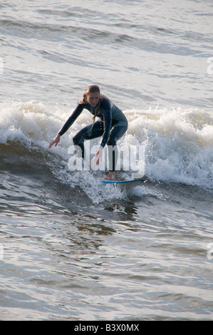 Young blonde woman wearing wetsuit surf sur surf sur les vagues au large de Aberystwyth, Pays de Galles, Royaume-Uni après-midi d'été Banque D'Images