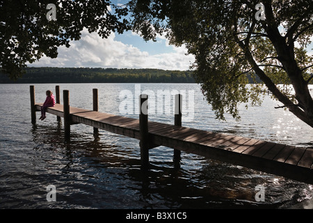 Enfant assis sur une jetée près de Sejs, lac Brassø, Jutland, Danemark Banque D'Images