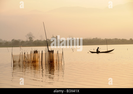 Pêcheur vietnamien dans un canot creusé sur le lac Lak Vietnam au lever du soleil Banque D'Images