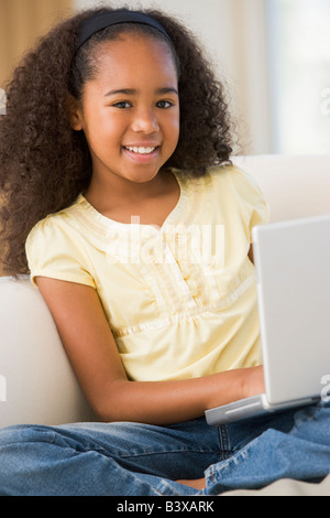 Jeune fille assise sur un canapé, à l'aide d'un ordinateur portable Banque D'Images