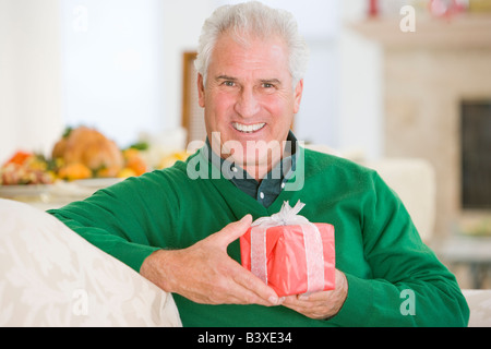 Senior Man Sitting on Sofa Holding A Christmas Gift Banque D'Images