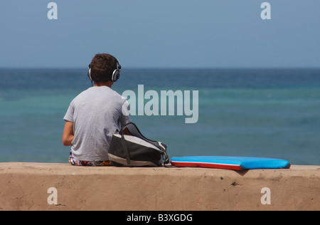 L'Espagnol teenage surfer portant des écouteurs et en attente de vagues à La Cicer, Playa de Las Canteras, à Las Palmas, Gran Canaria. Banque D'Images