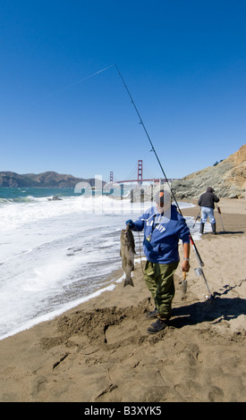 Un pêcheur nous tend un bar rayé À Baker Beach, à proximité du Golden Gate Bridge à San Francisco CA CALIFORNIE Banque D'Images