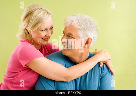 Portrait of smiling couple d'âge moyen en face de mur vert hugging Banque D'Images