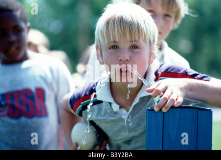 Jeune garçon de boire de l'eau d'une fontaine sur une cour d'école Banque D'Images