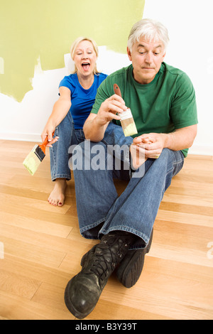 Couple d'âge moyen en face de wall ils sont la peinture vert tandis que homme essaie de peindre les ongles des femmes avec paintbrush Banque D'Images